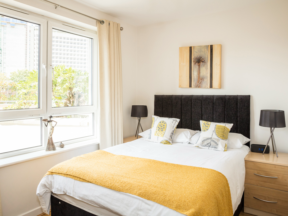 Sunlit master bedroom with double bed, yellow bedding, and large window at The Amber Suite, Woking