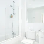Bathroom with overhead shower, bathtub, and white interior at The Amber Suite, Woking