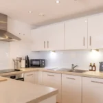 Contemporary open-plan kitchen with integrated oven and white cabinetry at The Sycamore Suite, Enterprise Place, Woking