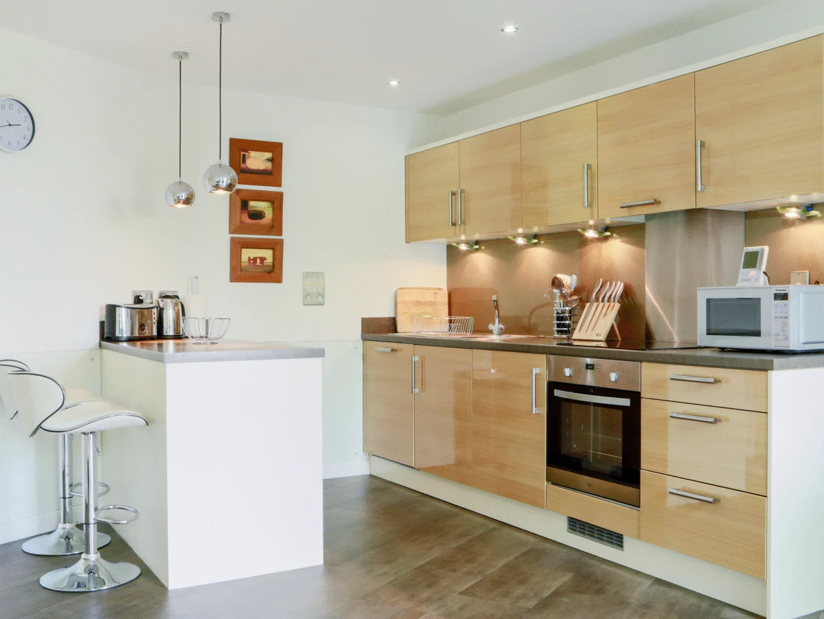 Contemporary open-plan kitchen with wood cabinetry, integrated appliances, and breakfast bar at The Willow Suite, Cardinal Place, Woking