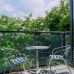 Glass-panel balcony with bistro table and chairs overlooking greenery at The Willow Suite, Cardinal Place, Woking