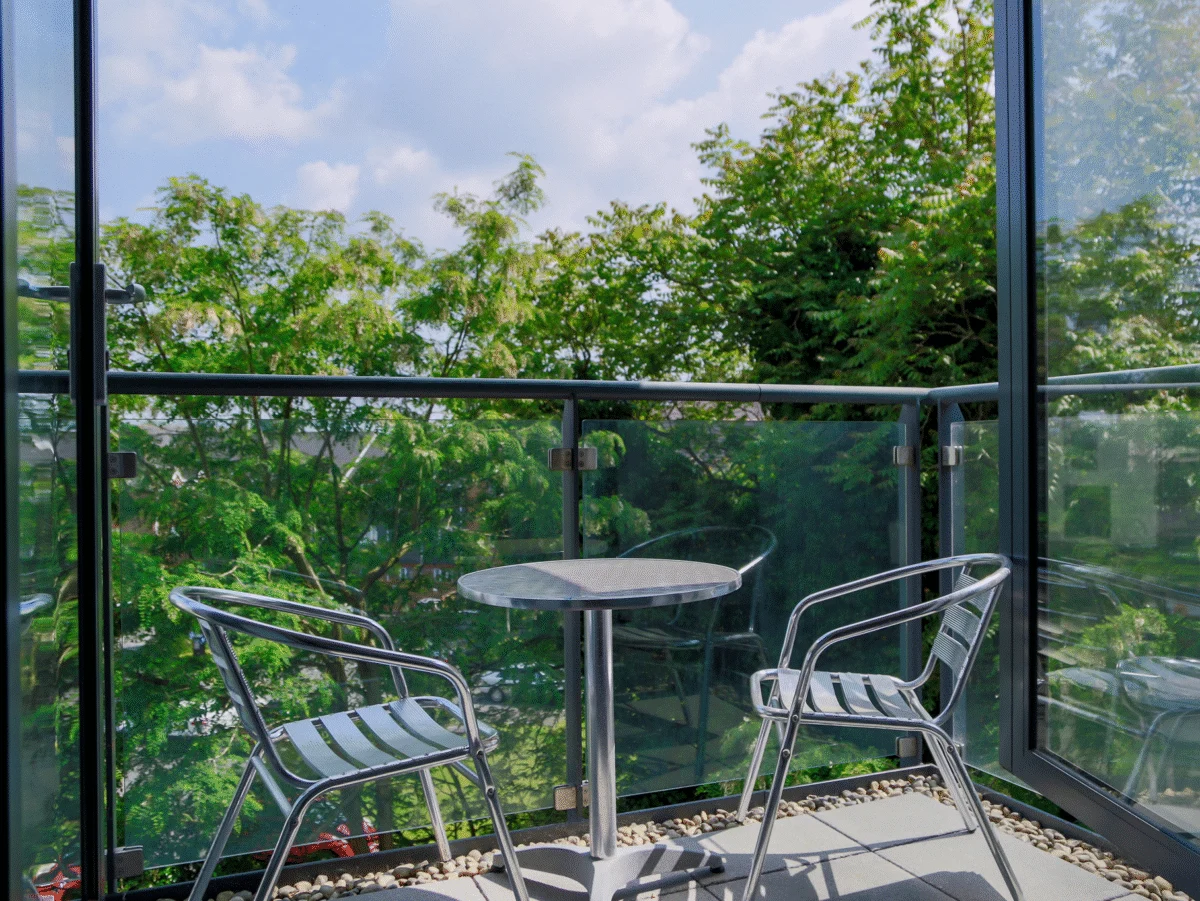 Glass-panel balcony with bistro table and chairs overlooking greenery at The Willow Suite, Cardinal Place, Woking
