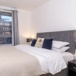 King bedroom with plush duvet, bedside lamps, and balcony view at The Sycamore Suite, Enterprise Place, Woking