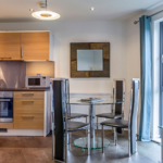 Modern kitchen and dining area with wood units, round table, and balcony door at The Willow Suite, Cardinal Place, Woking