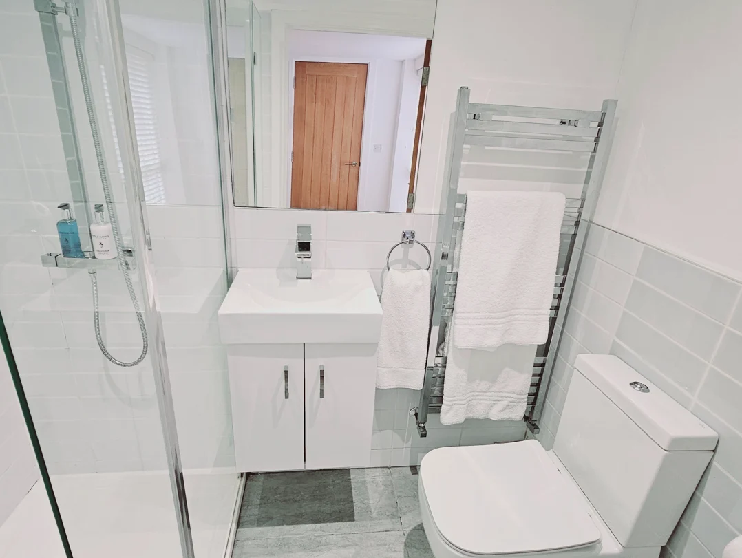 Modern white bathroom with shower, towel rack, and large mirror in The Oak Suite, Farnham