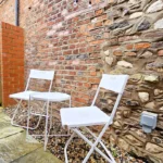 Outdoor patio seating against stone wall with two white chairs and table at The Oak Suite, Farnham