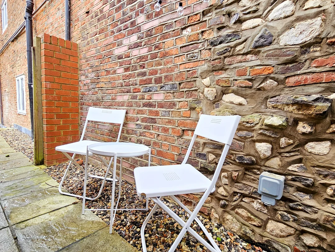 Outdoor patio seating against stone wall with two white chairs and table at The Oak Suite, Farnham