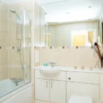 Second family bathroom with cream tiles, bath, and wide mirror at The Willow Suite, Cardinal Place, Woking”