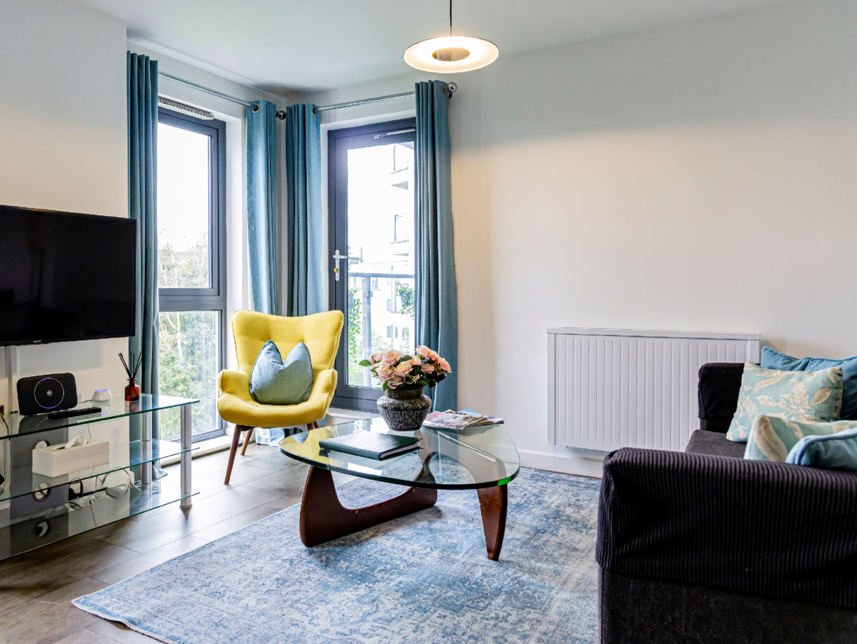 Spacious living room with TV, armchair, sofa, and large windows at The Willow Suite, Cardinal Place, Woking