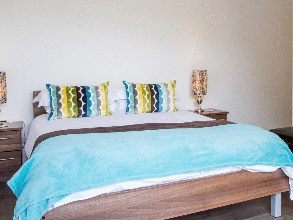 Stylish double bedroom with blue bedspread and accent cushions at The Willow Suite, Cardinal Place, Woking