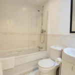 Modern bathroom with bathtub, overhead shower, toilet, and sink at The Daisy Suite, Centrium, Woking