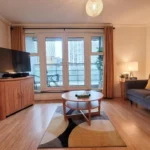 Spacious living room with TV, comfortable sofa, coffee table, and balcony doors at The Daisy Suite, Centrium, Woking