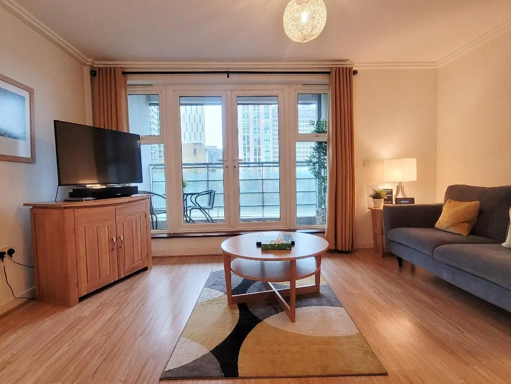 Spacious living room with TV, comfortable sofa, coffee table, and balcony doors at The Daisy Suite, Centrium, Woking