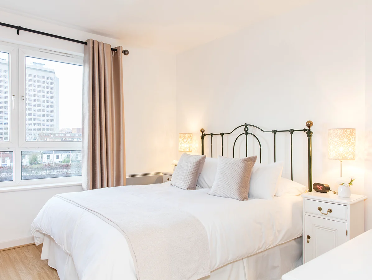 Sunlit twin bedroom with neutral décor and vibrant city backdrop at The Daisy Suite, Centrium, Woking